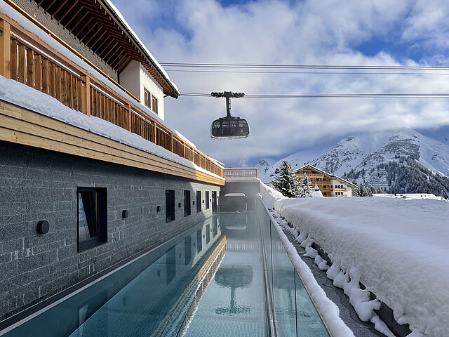 Aussenaufnahme Pool im Winter mit Seilbahn, die vorbei fährt, im Hintergrund